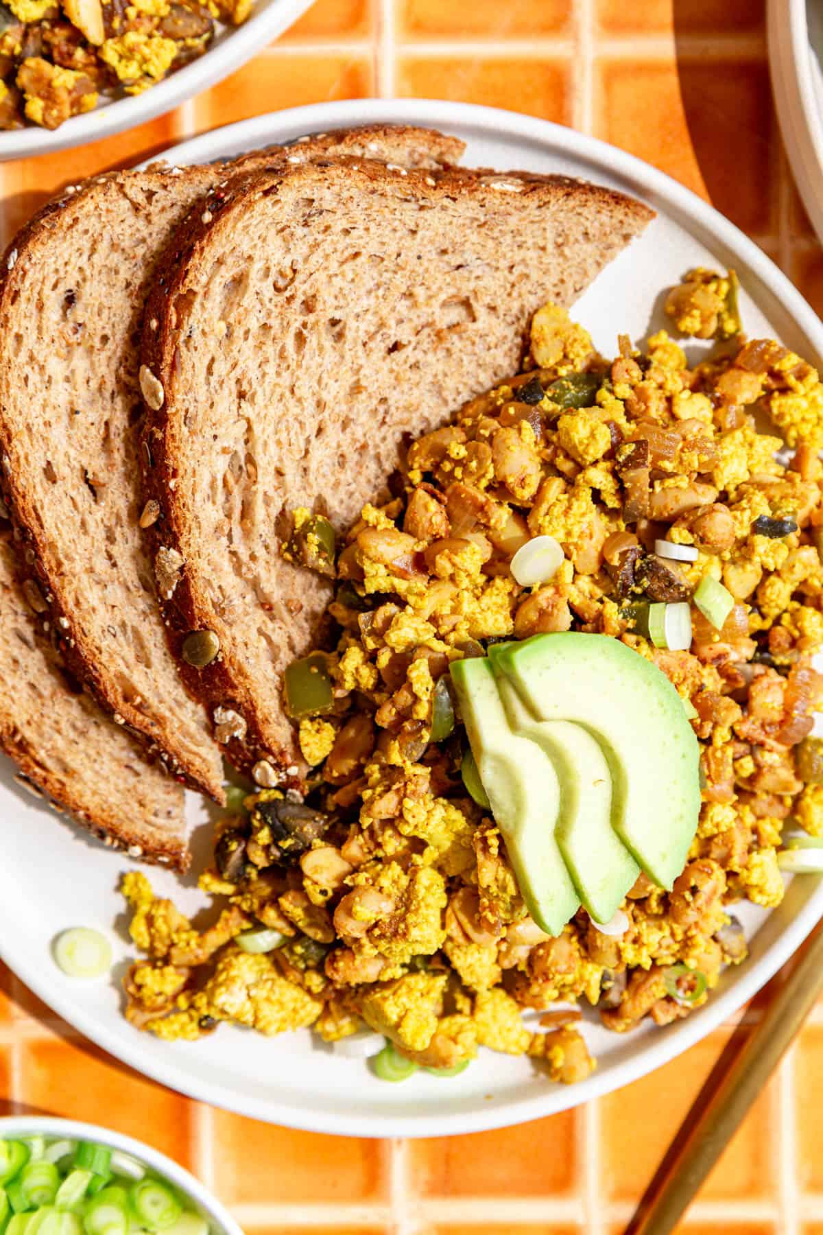 A plate of Scrambled Tempeh, topped with avocado, and served with toast.