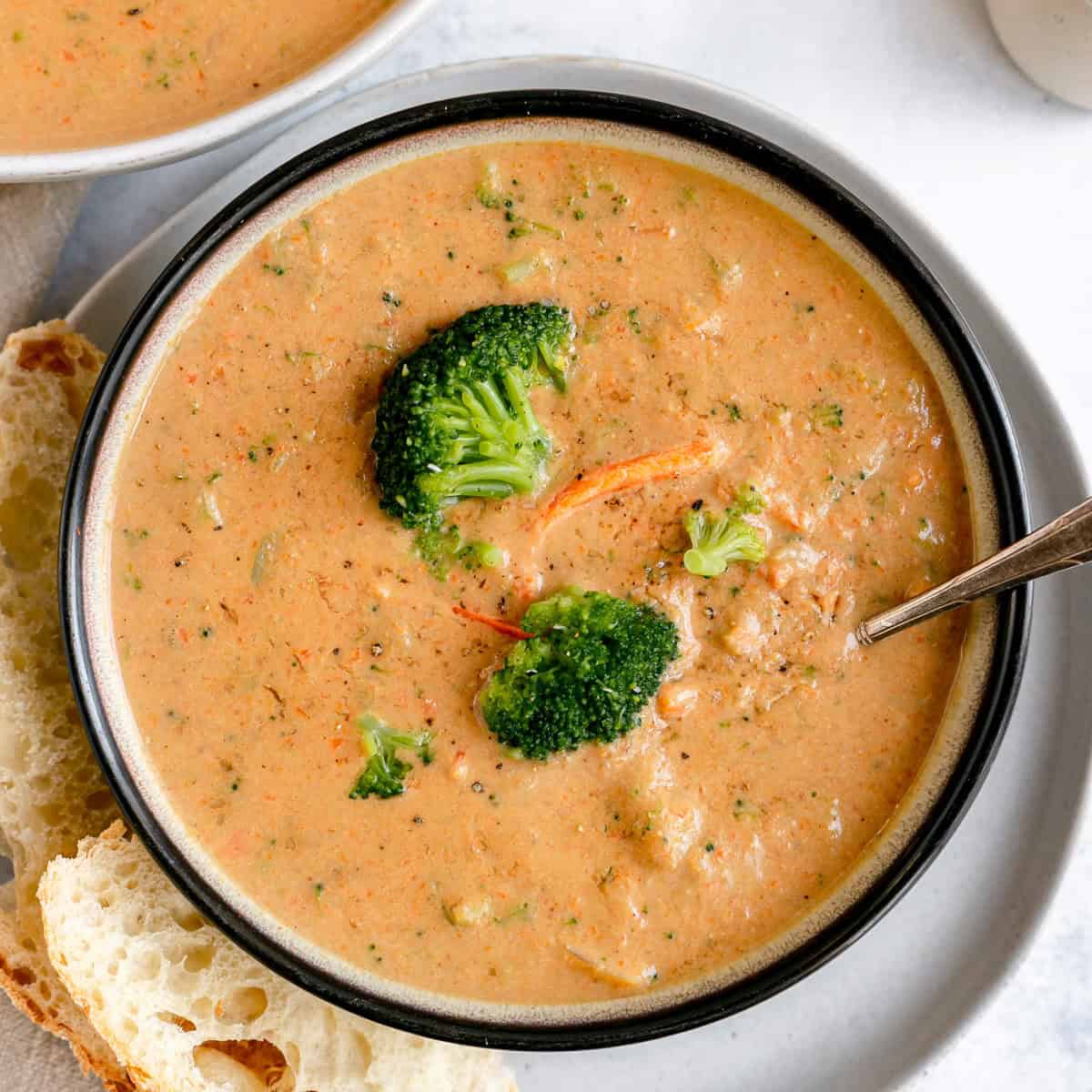 A bowl of vegan broccoli cheddar soup with a spoon and two slices of crusty bread.