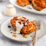 A twice baked sweet potato on a plate, topped with non-dairy yogurt and coconut bacon.