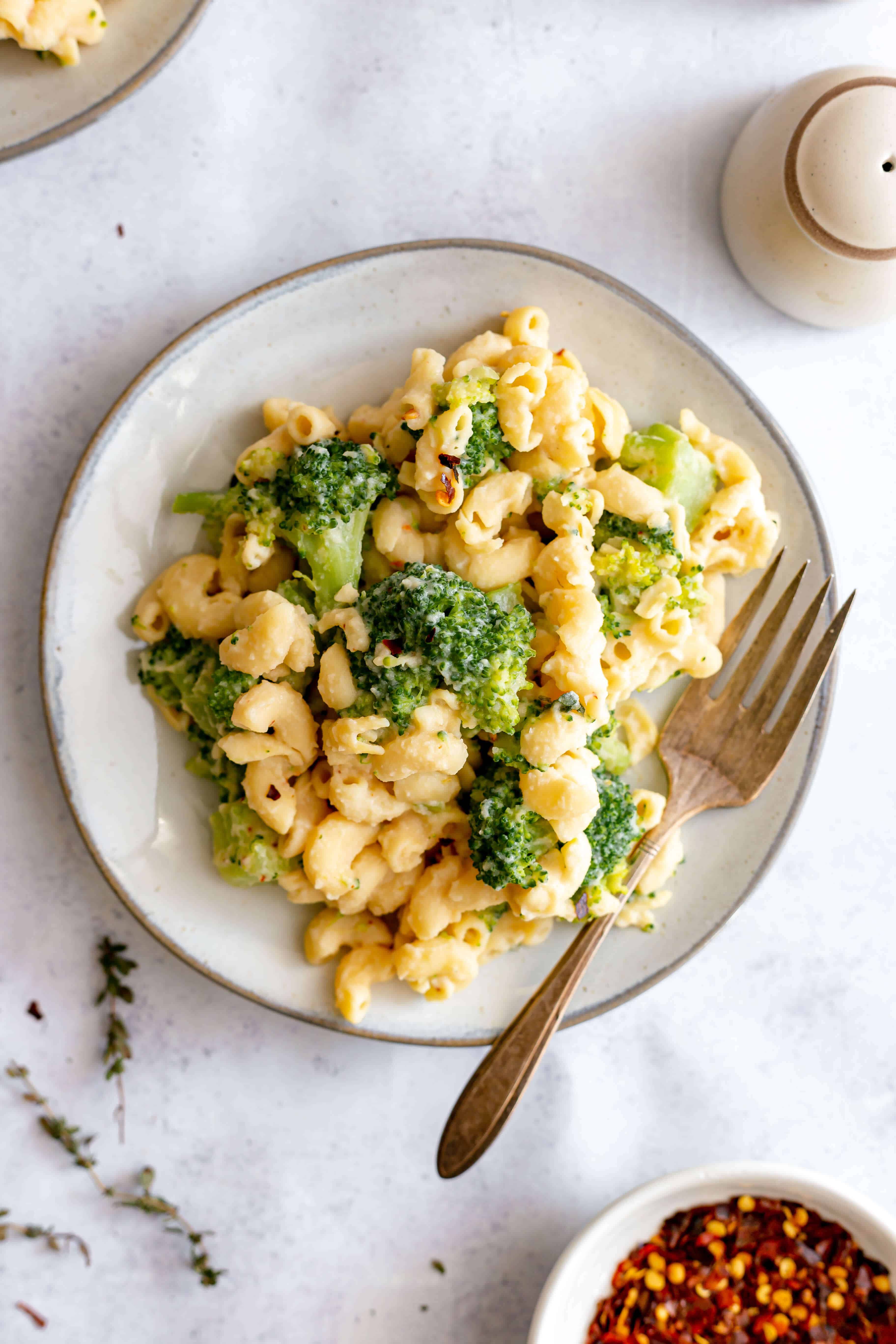 A plate of vegan broccoli mac and cheese with red pepper flakes and fresh thyme.