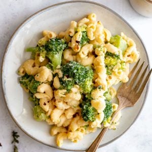A plate of vegan broccoli mac and cheese with red pepper flakes and fresh thyme.