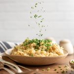 Fresh chives being sprinkled onto a bowl of vegan mashed potatoes.