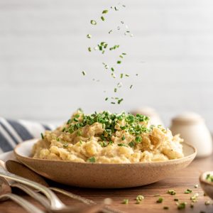 Fresh chives being sprinkled onto a bowl of vegan mashed potatoes.