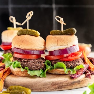 Two vegan sliders served with lettuce, tomato, onion, and pickles.