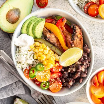A fajita bowl with mushrooms, peppers, beans, tomatoes, corn, avocado, and vegan sour cream.