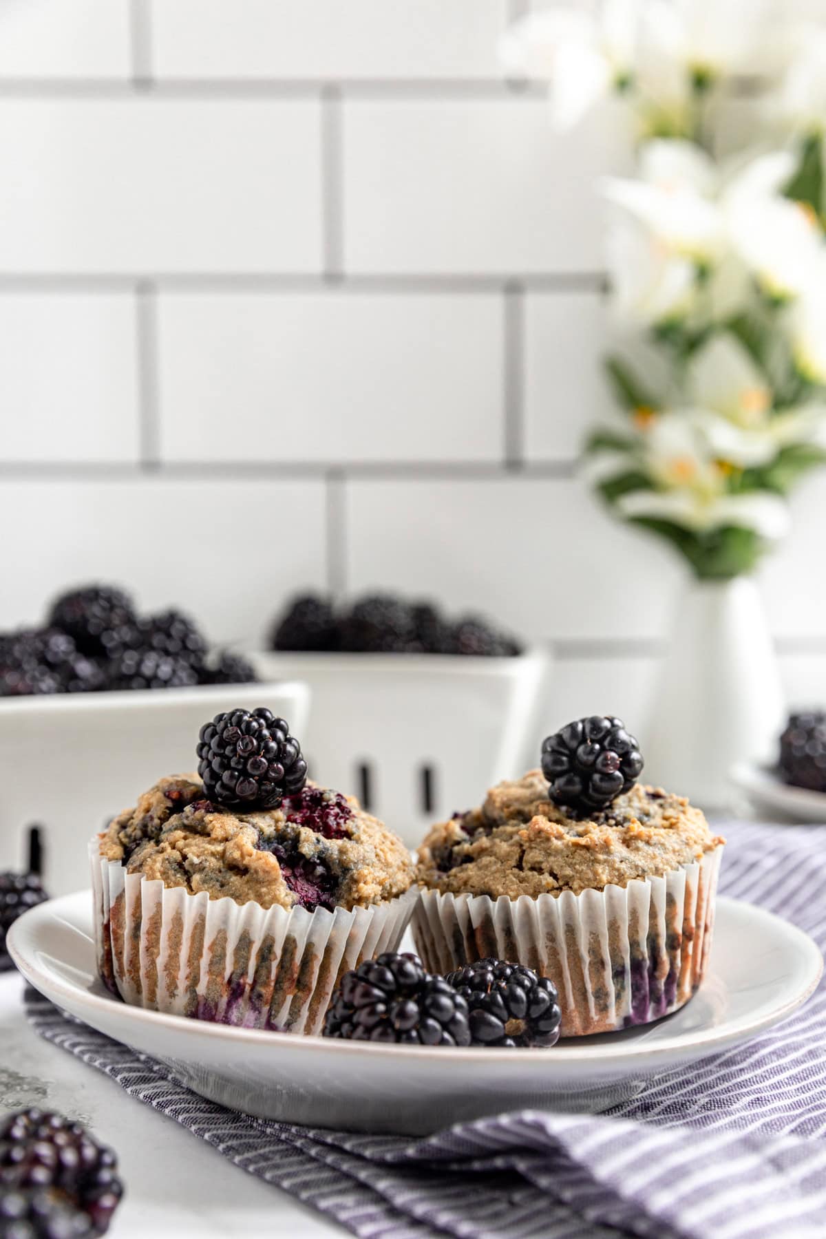Two Vegan Blackberry Muffins on a plate, topped with blackberries.