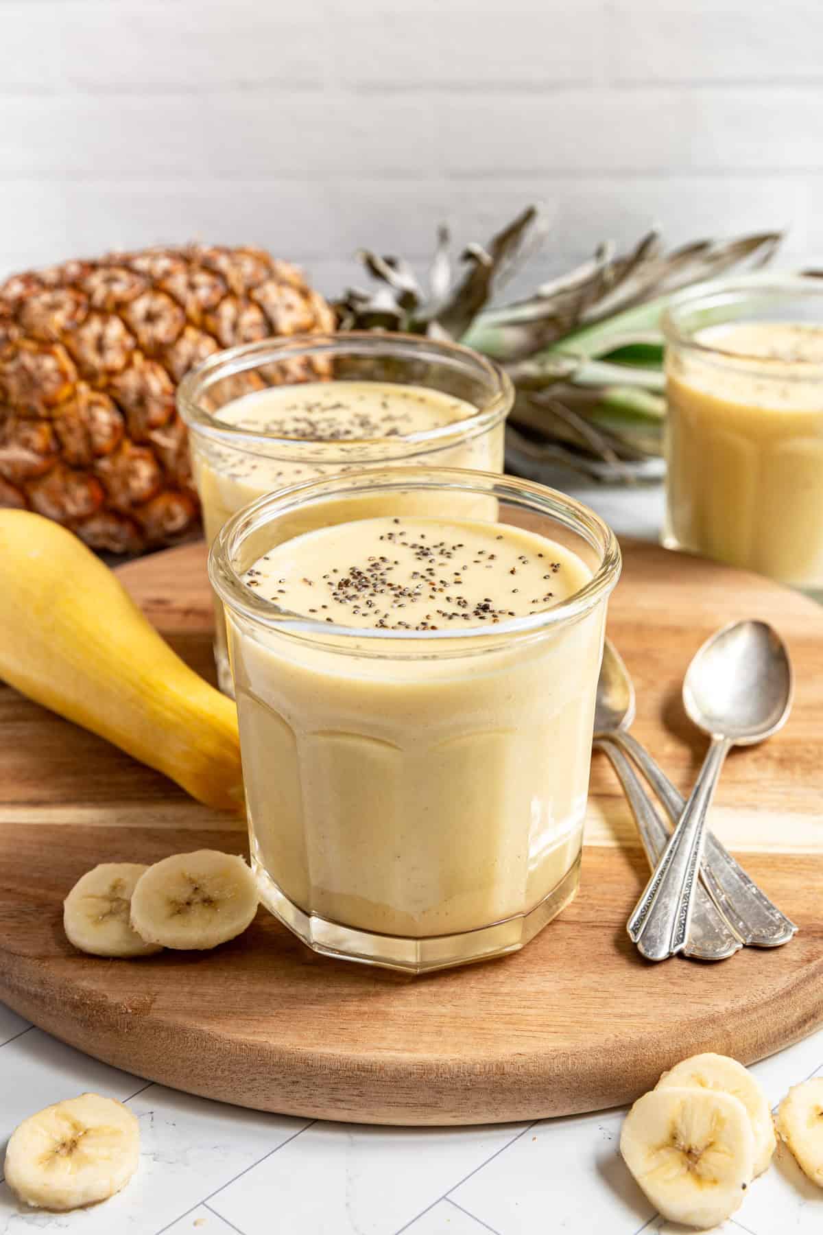 A glass of Summer Squash Smoothie on a platter surrounded by pineapple, squash, and banana.q