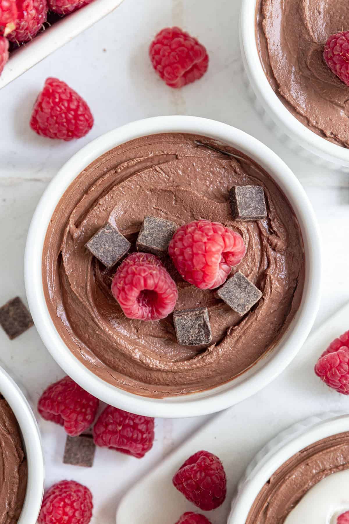 An overhead view of a ramekin of Vegan Tofu Chocolate Mousse topped with chocolate chunks and raspberries.