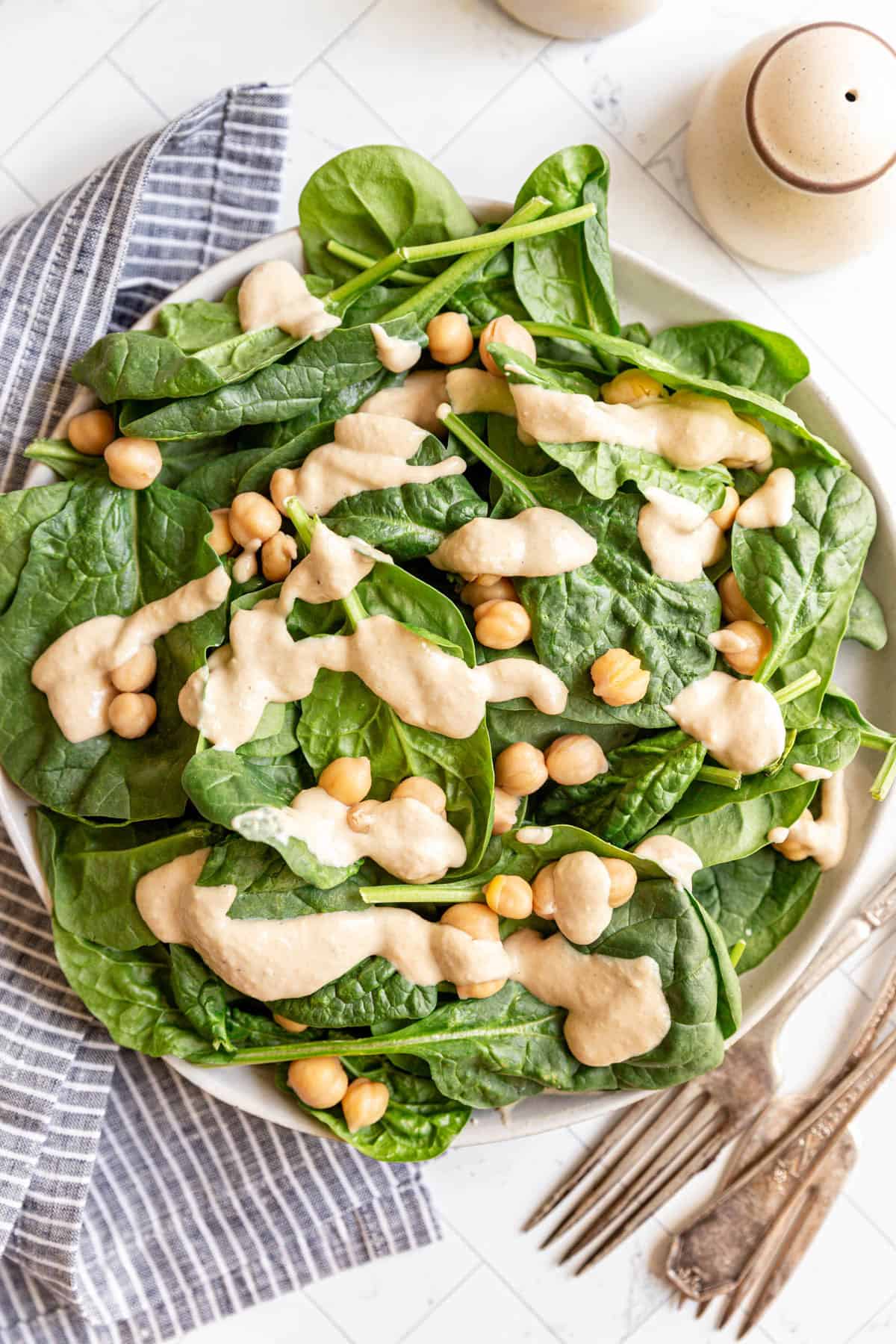 A spinach salad dressed with Vegan Chickpea Dressing.