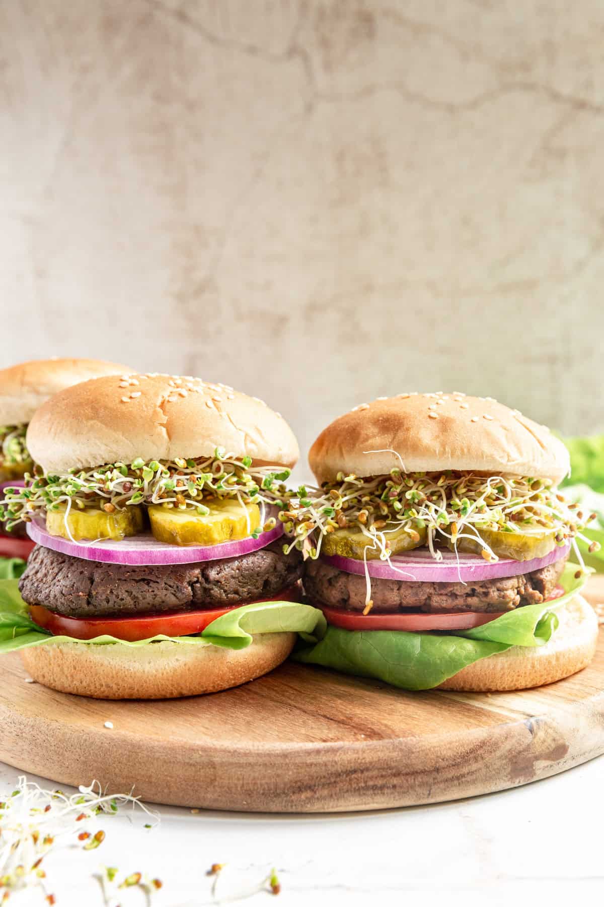 Two Vegan High Protein Seitan Burgers loaded with lettuce, tomatoes, onions, pickles, and microgreen sprouts, served on sesame seed buns.