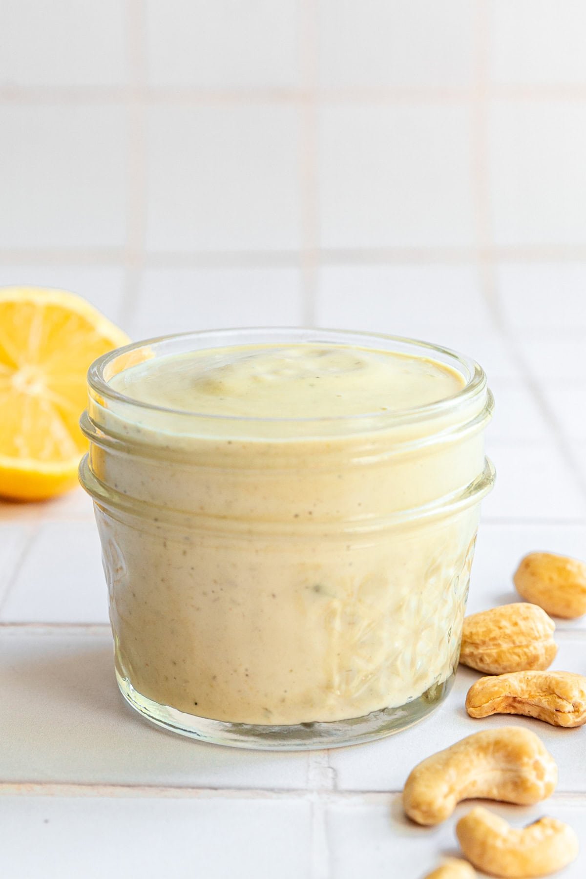 A jar of Vegan Oil-Free Cashew Caesar Salad Dressing with cashews and lemons.