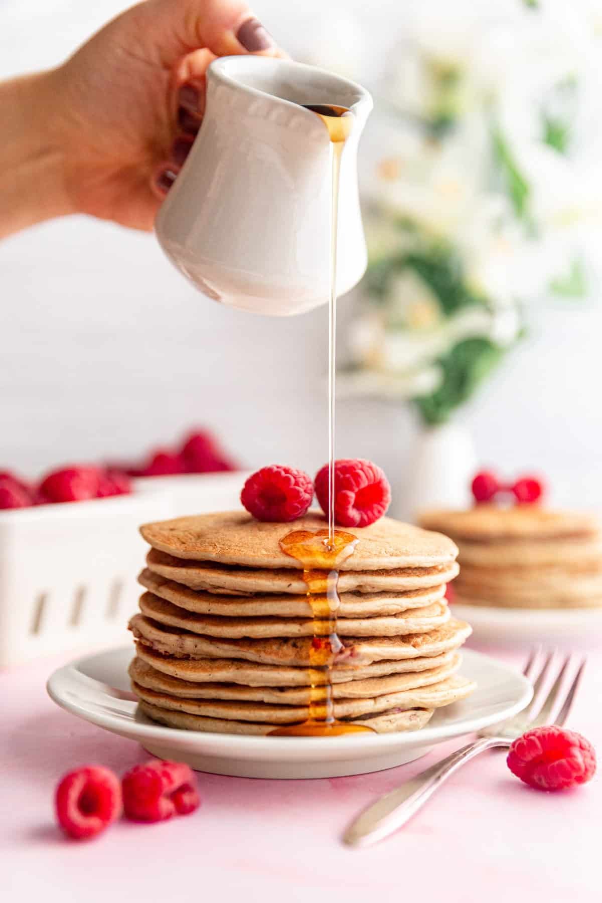 Drizzling maple syrup onto Vegan Raspberry Lemon Pancakes