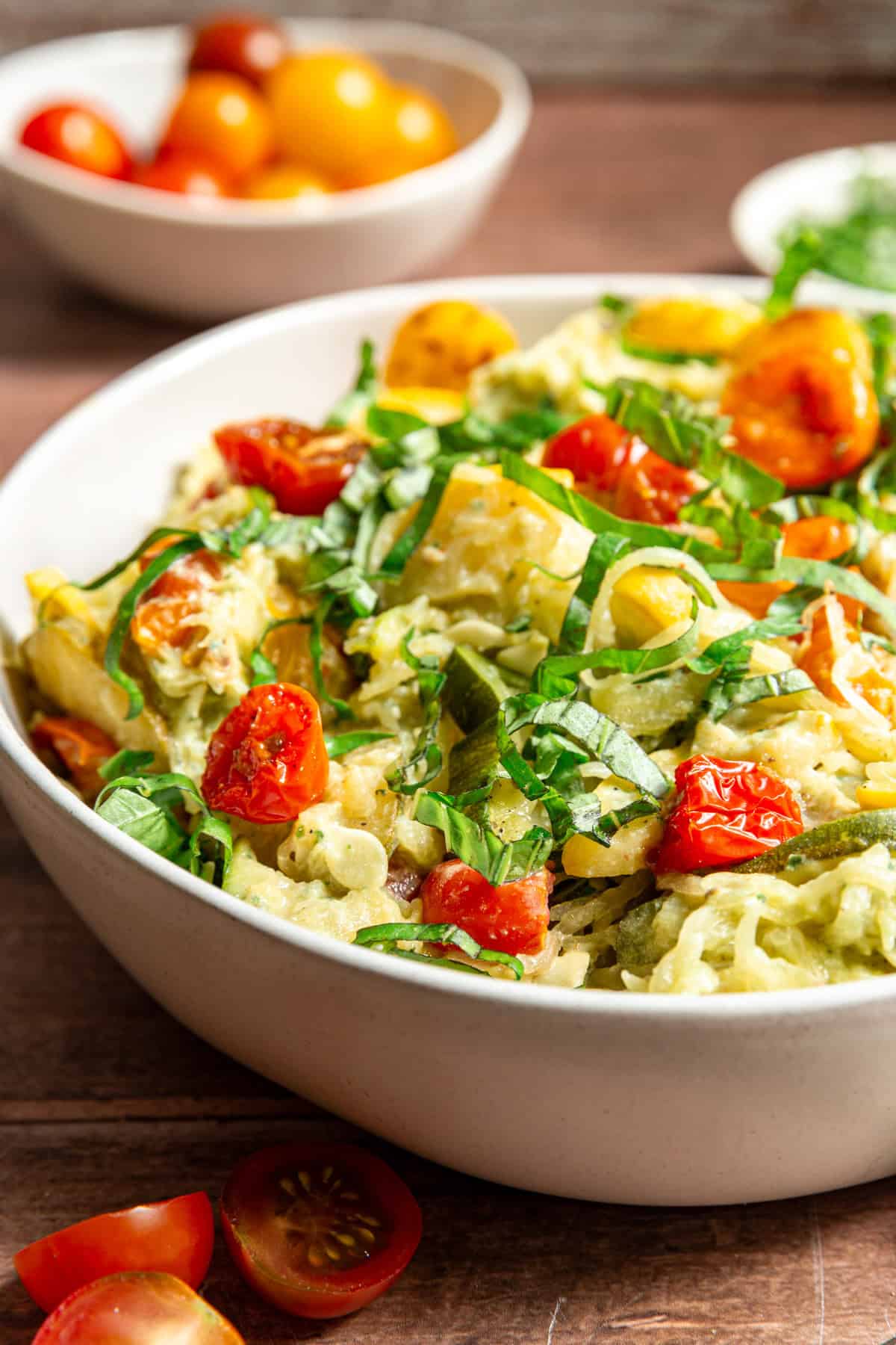 A bowl of Creamy Vegan Pesto Spaghetti Squash with Roasted Tomatoes & Zucchini, garnished with fresh basil.