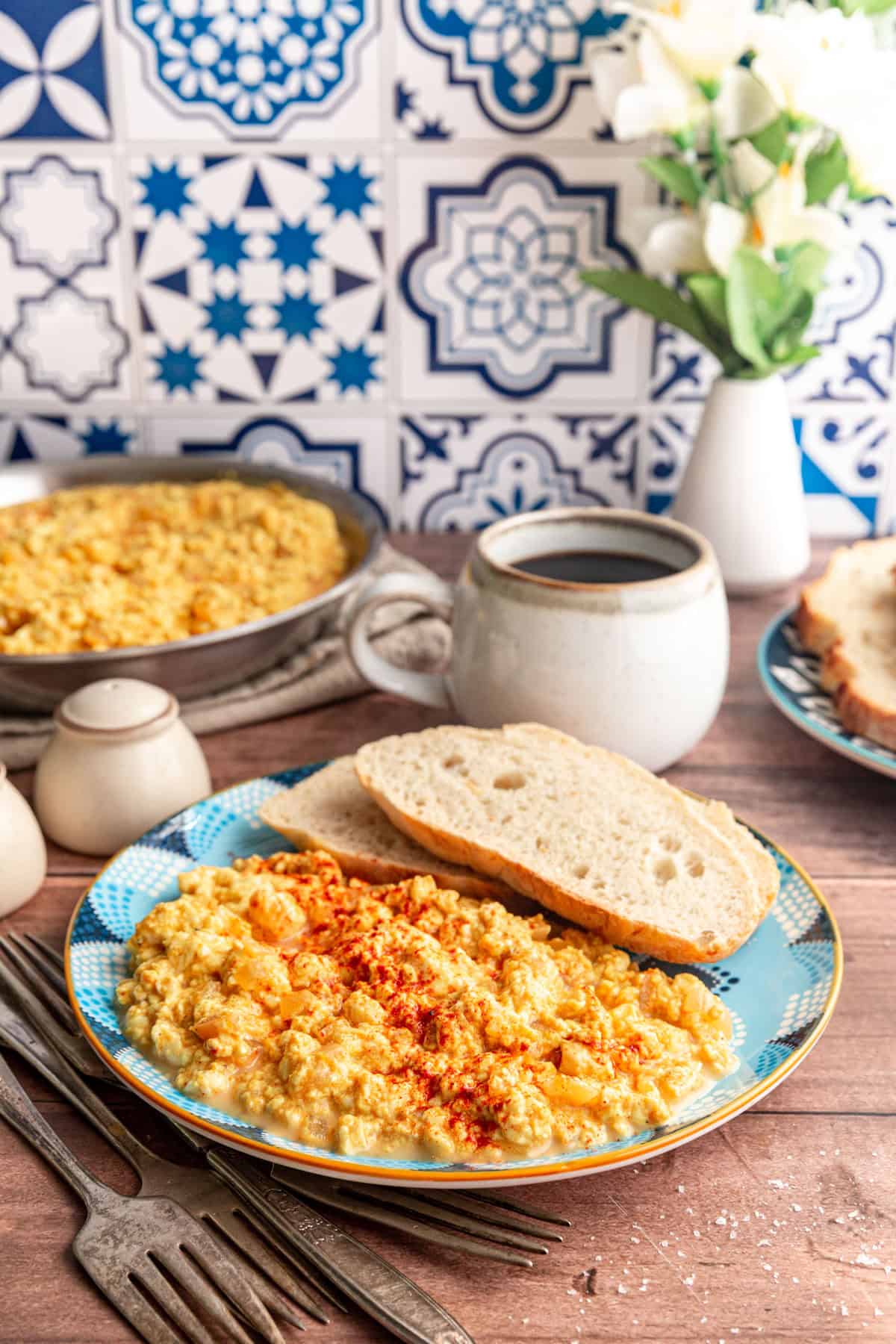 A breakfast table set with Silken Tofu Scrambled Eggs, toast, coffee, and a vase of flowers.
