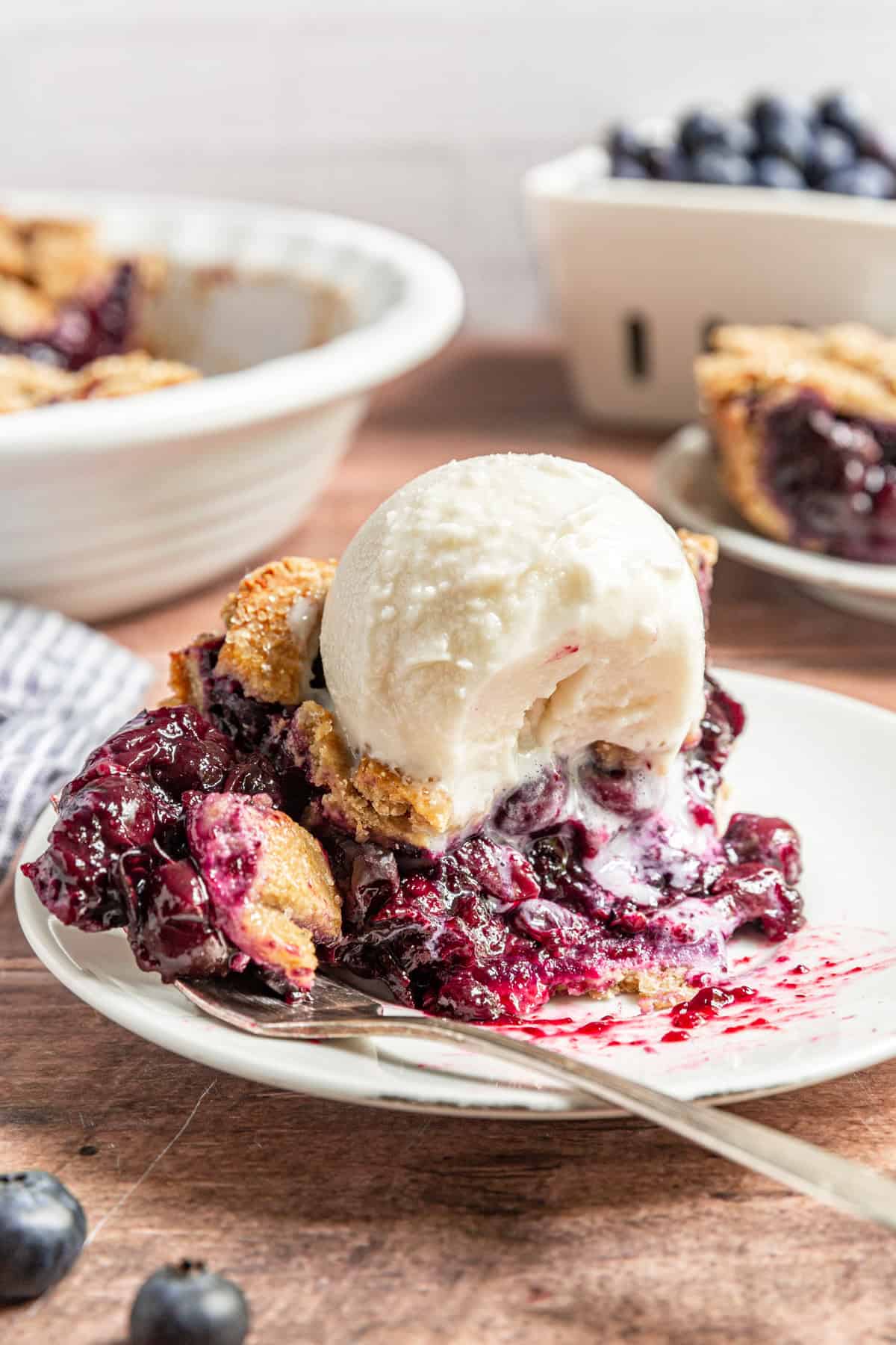 A slice of Gluten Free Vegan Blueberry Pie with a bite taken and ice cream melting into the filling.