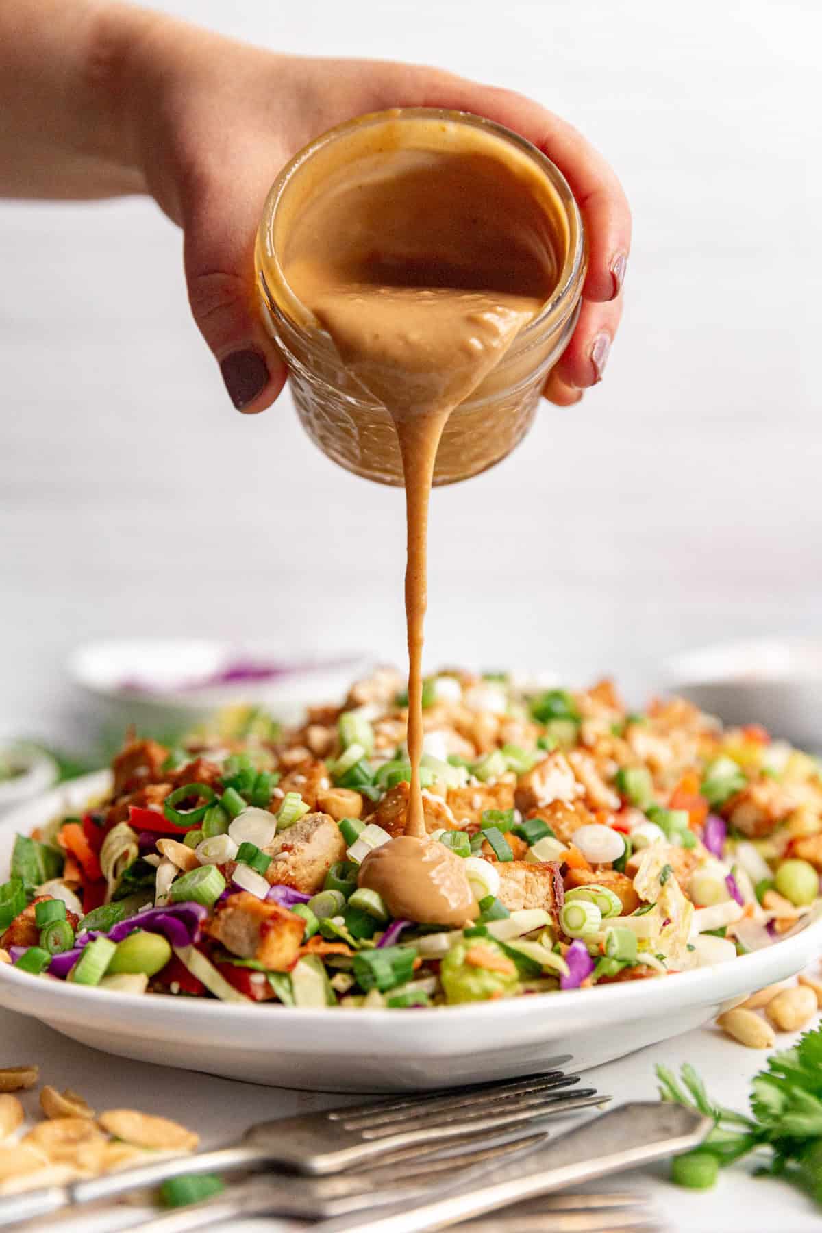 Healthy Peanut Sesame Dressing being poured onto Thai Peanut Salad.