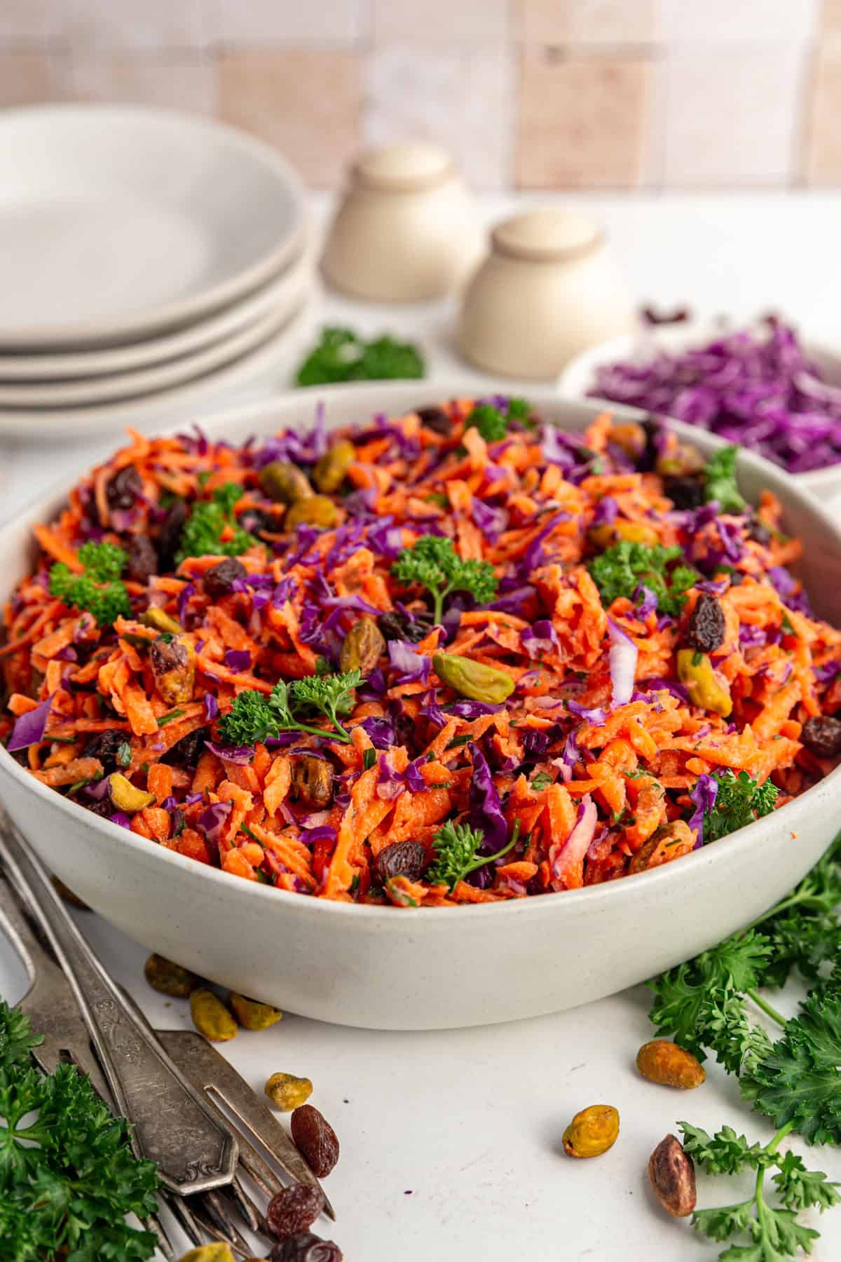 A bowl of Carrot Raisin Salad with a stack of plates, ready to serve.