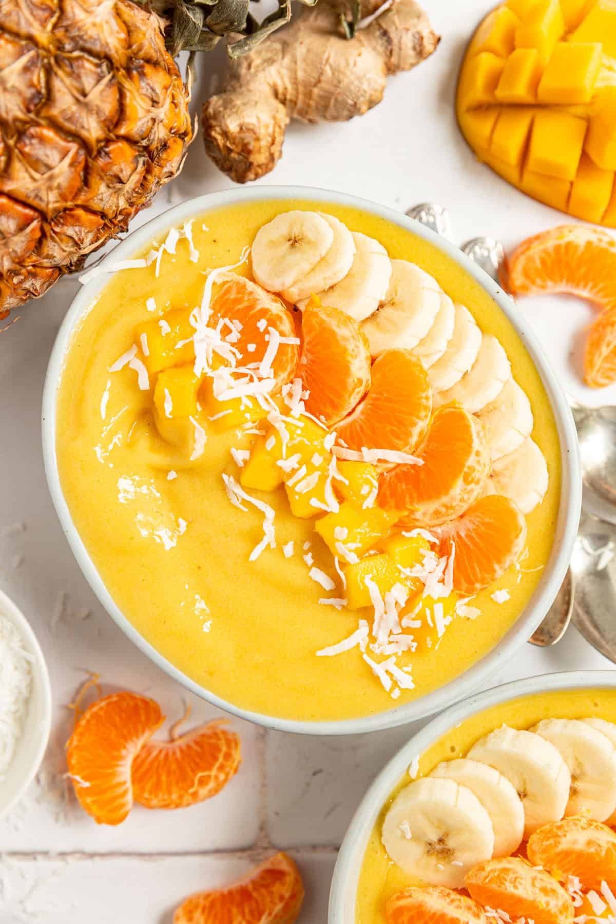A Tropical Orange Smoothie Bowl surrounded by fresh pineapple, mango, ginger, and cuties.