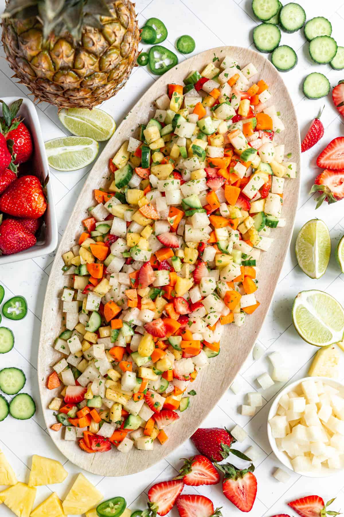 A platter of Jicama Pineapple Slaw surrounded by fresh strawberries, cucumbers, jicama, and pineapple.