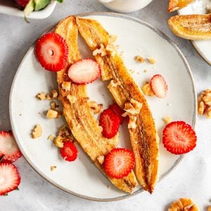 A plate of vegan air fryer bananas topped with strawberries and walnuts.