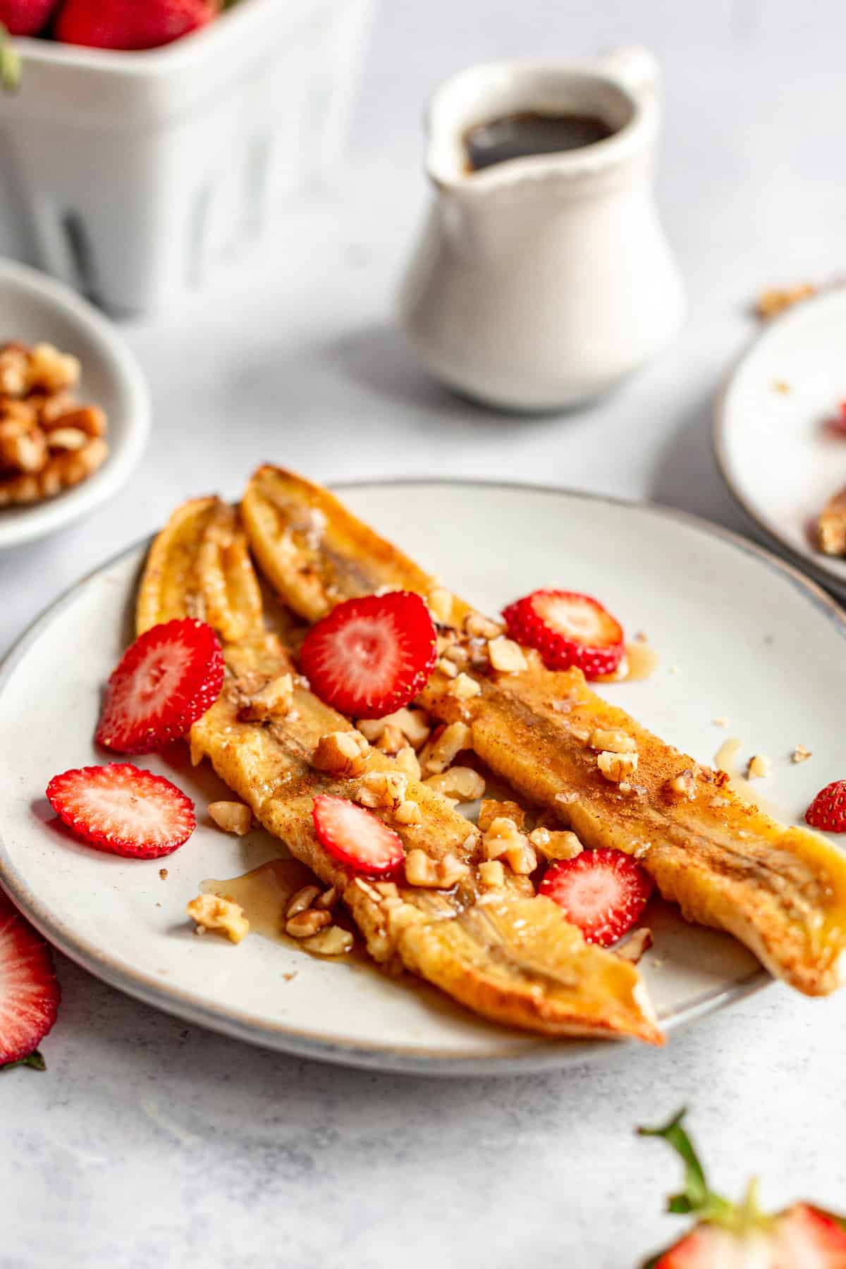 A plate of vegan air fryer bananas topped with strawberries and walnuts.