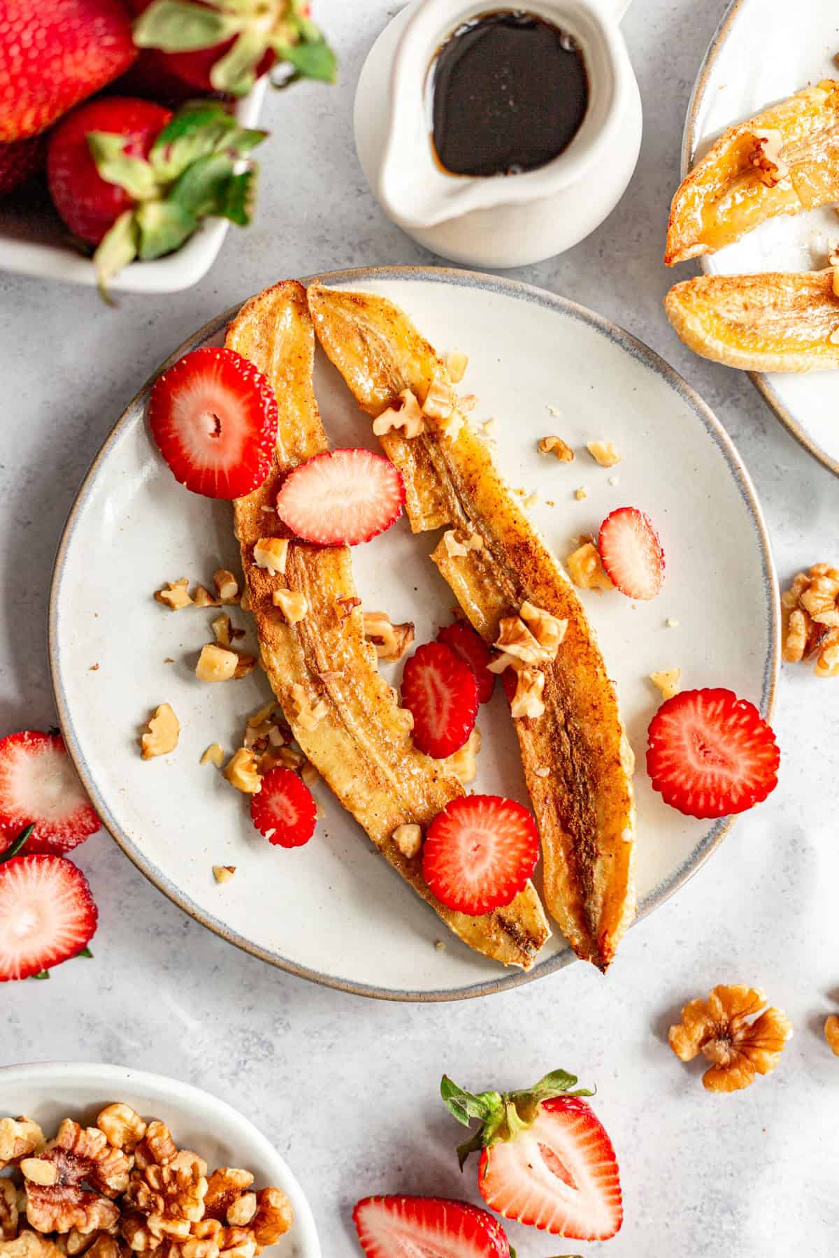 A plate of vegan air fryer bananas topped with strawberries and walnuts.