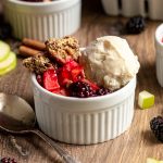 A ramekin with apple blackberry crumble and a scoop of ice cream.