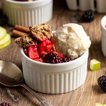 A ramekin with apple blackberry crumble and a scoop of ice cream.