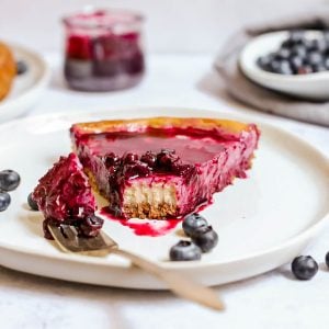 A slice of baked blueberry cheesecake with a bite taken out.