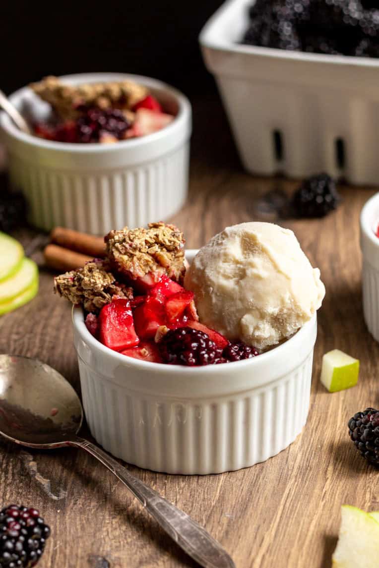 A ramekin with apple blackberry crumble and a scoop of ice cream.