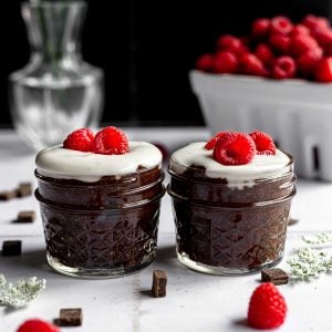 Two jars of cold brew coffee chia pudding topped with vegan yogurt and raspberries.
