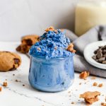 A jar of blue cookie dough, topped with crumbled cookies.
