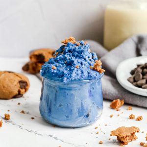 A jar of blue cookie dough, topped with crumbled cookies.