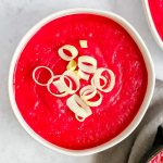 A bowl of bright pink creamy vegan beet soup, garnished with sliced leeks.