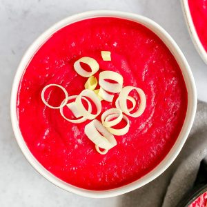 A bowl of bright pink creamy vegan beet soup, garnished with sliced leeks.