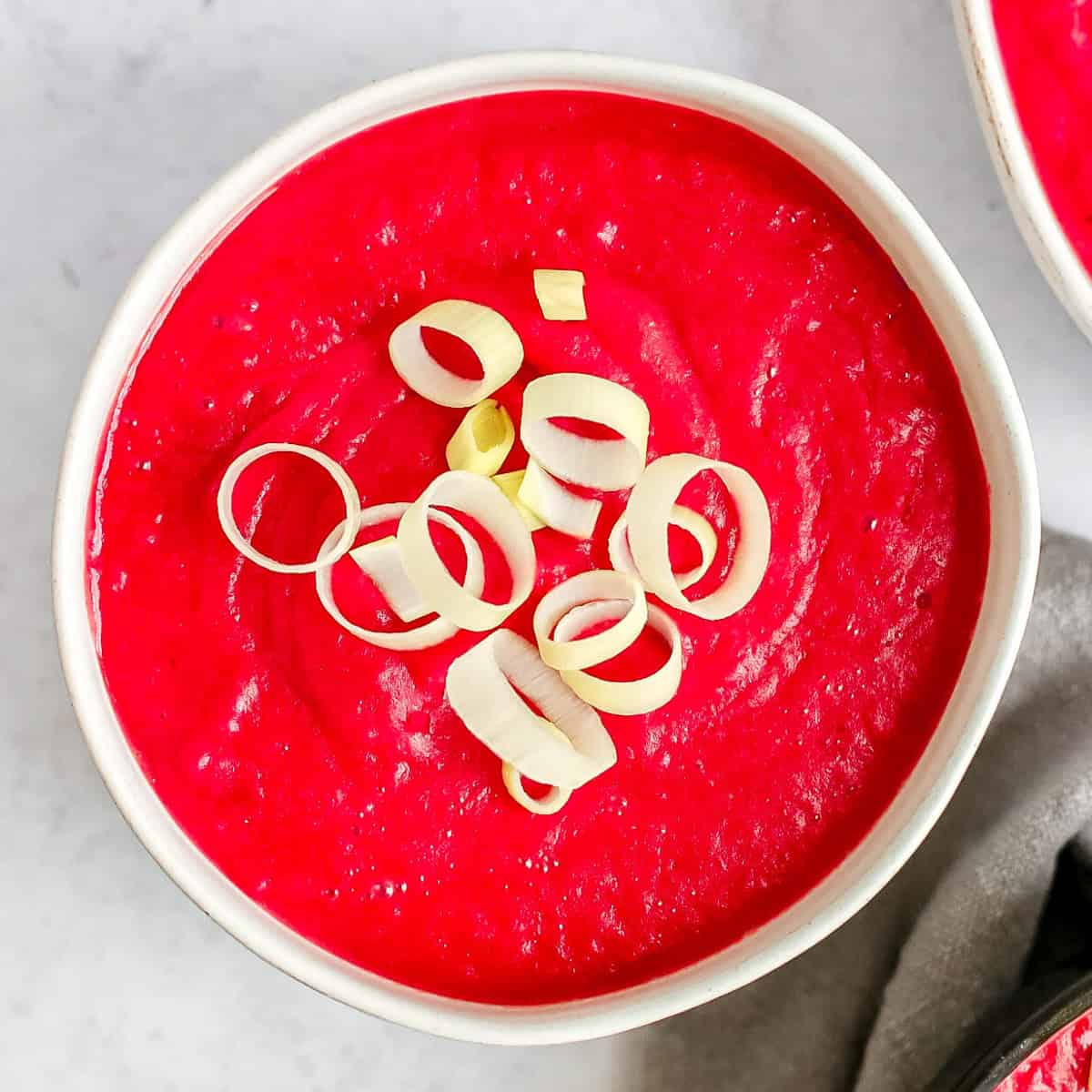 A bowl of bright pink creamy vegan beet soup, garnished with sliced leeks.