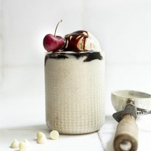 A glass filled with date sweetened no churn vegan vanilla ice cream, drizzled with date syrup and topped with a cherry.