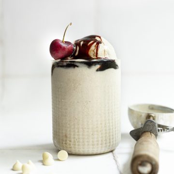 A glass filled with date sweetened no churn vegan vanilla ice cream, drizzled with date syrup and topped with a cherry.