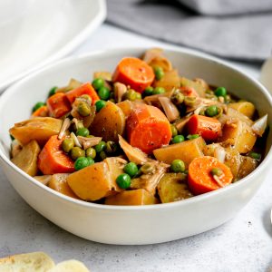 A bowl of vegan beef stew with potatoes and peas.