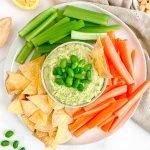 A bowl of edamame hummus on a platter, with vegetables.
