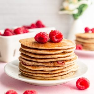 A stack of vegan raspberry lemon pancakes, topped with raspberries.