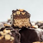 A vegan snickers bar sliced in half to reveal the nougat, date caramel, and peanuts inside.