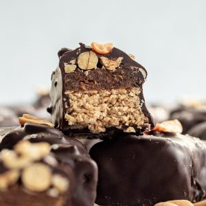 A vegan snickers bar sliced in half to reveal the nougat, date caramel, and peanuts inside.