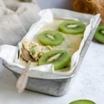 A container of kiwis and cream ice cream with a spoon scooping some out.