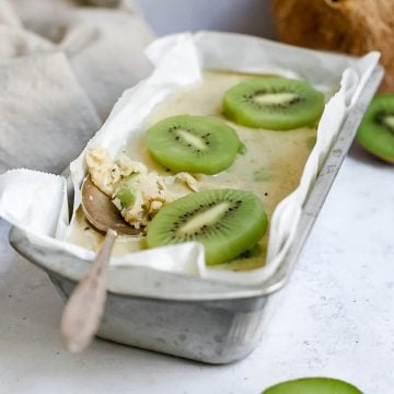A container of kiwis and cream ice cream with a spoon scooping some out.