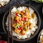 A bowl of kung pao tempeh with chopsticks, served over rice.