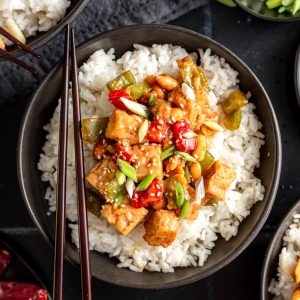 A bowl of kung pao tempeh with chopsticks, served over rice.
