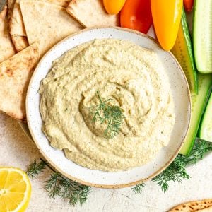 A bowl of lemon dill hummus, served with cucumbers, peppers, and pita.