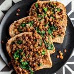 A plate with three slices of lentils and greens toast.