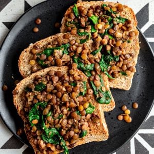 A plate with three slices of lentils and greens toast.